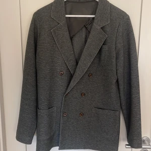 Grön dubbelknäppt kavaj John Henric - Snygg grön dubbelknäppt kavaj från John Henric med fyra bruna knappar framtill. Tillverkad i bomull och nylon, med slät grön insida. Perfekt för en stilren look på sommaren.