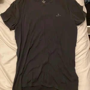 Svart t-shirt från GANT i bomull - Svart t-shirt från GANT i storlek M med diskret logga på bröstet. Klassisk rund hals och korta ärmar, tillverkad i mjuk bomull som känns skön mot huden. Perfekt för dig som gillar stilrena och enkla plagg med snygg passform. Skick är inte helt hundra och säljs därför väldigt väldigt billigt! 