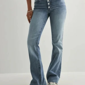 Blå midwaist jeans från Nelly, bootcut - Snygga blå jeans från Nelly med midwaist och bootcut passform. Jeansen har flera silverfärgade knappar framtill och klassiska bakfickor. Tillverkade i mjukt denimtyg som ger en skön känsla och stilren look.