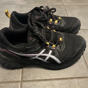 ASICS Trail Scout 3 svarta löparskor - Svarta ASICS Trail Scout 3 löparskor med rosa och vita detaljer samt gula dragflikar. Grov sula för extra grepp. Strl 38,  24 cm