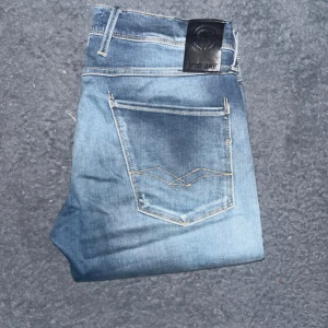 Replay Anbass jeans  - Säljer ett par Replay Anbass jeans i klassisk blå tvätt med snygga slitningar och hål och råa kanter vid bensluten. Jeansen har fem fickor, guldfärgade sömmar och en cool detalj på bakfickorna. Perfekt passform och riktigt skön stretch i materialet. Längd 91cm, midja 43cm. L storleken är okänd men jag bedömer den till en kort L30 alternativt långa L28. JAG SKICKAR INGA FLER BILDER NÄR JAG BÄR JEANSEN :) (7)