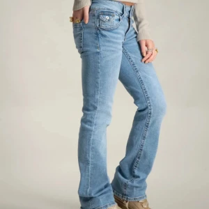 Ljusblå bootcut jeans från Levis - Säljer ett par ljusblå Gina jeans med bootcut passform. Klassisk femficksmodell med låg midja och raka ben som släpper ut lite vid ankeln. Jeansen är i mjukt denimtyg och har snygga detaljer på bakfickorna. Perfekta för en chill och trendig look.