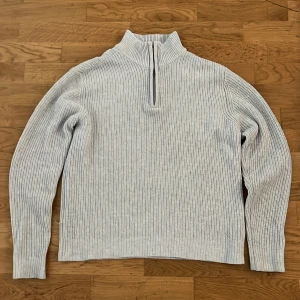Ljusgrå stickad half zip-tröja 157 - Säljer en ljusgrå stickad tröja från 157 med ribbad struktur och half zip-dragkedja vid halsen. Tröjan har långärmade ärmar och hög krage som ger en chill och snygg look. Perfekt för dig som gillar enkel och stilren design.