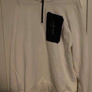 Vit Sail Racing half zip tröja XL - Vit långärmad tröja från Sail Racing i storlek XL. Tröjan har en svart half zip framtill och en svart bröstficka med dragkedja och logga. Materialet är mjukt och känns som bomull, perfekt för chill dagar. Snygg detalj med loggan även på ryggen.