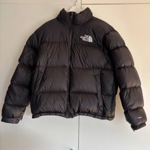 The North Face Retro Nuptse 1996 Dunjacka (M) - Säljer en svart dunjacka från The North Face, modell Retro Nuptse 1996. Den är i mycket gott skick! Säljer den för att den tyvärr är för liten för mig. Passar utmärkt nu till vintern! Tveka inte att skicka ett meddelande om du har några frågor😊 Mått: bredd 57 cm, längd 62 cm, armlängd 56 cm