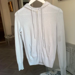 Ljusblå hoodie i kashmir från Soft Goat - Säljer min super fina ljusblå kashmir cardigan från soft goat. Tröjan säljs heller inte längre i denna ljusblå färg på hemsidan. Den har några skador som en fläck på armen och ett litet hål längst ner. Fickan på insida har även släppt vid ena tråden men man ser det inte på utsidan och det påverkar inte fickans funktion. Original pris ca 2700kr