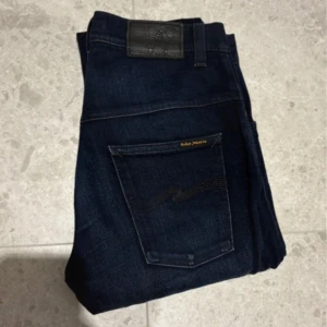 Mörkblå jeans från Nudie Jeans - Snygga mörkblå jeans från Nudie Jeans i modellen thin finn. Storlek W30 L32 och passformen är slim. Snygga vikningar fram och bak och använd ett fåtal gånger. Säljer dem för att de har blivit för tajta i midjan och tveka inte att höra av er vidfunderingar.                       pris går att diskuteras!