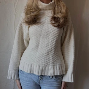 Vit stickad polotröja - Vit stickad polotröja med bred ribbad krage och muddar. Tröjan har ett snyggt strukturerat mönster i zigzag och är långärmad med relaxed fit. Perfekt till jeans för en snygg och mysig höstoutfit.