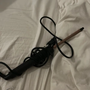 Locktång med konisk stav - Praktisk locktång med konisk stav för snygga lockar. Utrustad med enkel on/off-knapp och lång sladd. Svart handtag och kopparfärgad stav. Gott skick utan synliga defekter eller slitage.