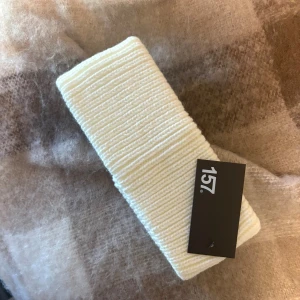 Vit ribbad stickad pannband  - Snyggt vitt ribbat stickat pannband från 157, perfekt för att hålla öronen varma under kyliga dagar. Stilren design med bred form och mjukt material som sitter skönt på huvudet. Passar dig som gillar enkel och clean look.