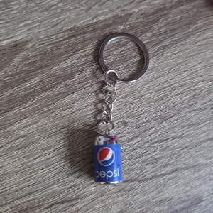Pepsi nyckelring - Nyckelring med en miniatyrburk av Pepsi. Perfekt för samlare eller som en rolig accessoar till nycklar eller väska. Produkten ser ut att vara i mycket gott skick utan synligt slitage.