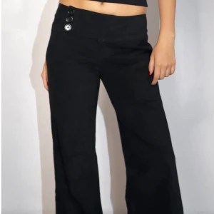 Svarta vida byxor med knappar - Snygga svarta byxor med låg midja och vida ben. Byxorna har tre dekorativa knappar framtill i midjan. Endast använda en gång! Står att de är i M men skulle säga S/M