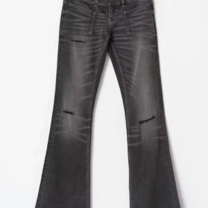 Grå bootcut jeans med slitningar - Snygga grå jeans med bootcut passform och låg midja. Jeansen har slitna detaljer på låren och knäna samt stora framfickor. Perfekta för en trendig och avslappnad look.