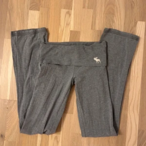 Grå mjukisbyxor Abercrombie & Fitch XS - Snygga grå mjukisbyxor från Abercrombie & Fitch i storlek XS. Byxorna har bred, hög midja med logotypen 'Abercrombie' broderad framtill och en liten älg på sidan. Mjukt bomullsmaterial och raka ben för chill och avslappnad stil.