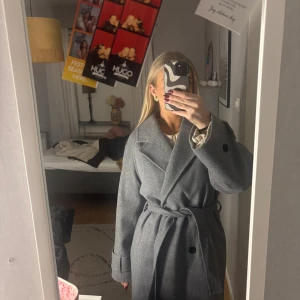 Grå lång kappa  - Kappa från Nelly som inte säljs längre, knappt använd som ny. Den har även slits där bak. Skriv för mer bilder🩷.                            