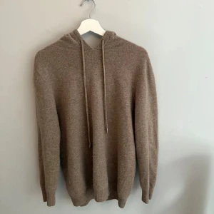 Beige Kashmir hoodie med huva - Mysig beige stickad hoodie med huva och snörning. Tröjan har lång ärm och ribbade muddar vid ärmslut och nederkant. Nypris 1200 italienskt märke. Mitt pris 699