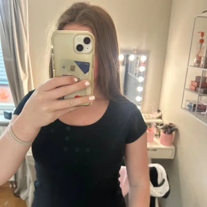 Svart basic topp från 157 - En svart, enkel och stilren topp från 157 med rund halsringning och korta ärmar. Tillverkad i mjuk bomull som känns skön mot huden. Perfekt att matcha med jeans eller kjol för en clean look.