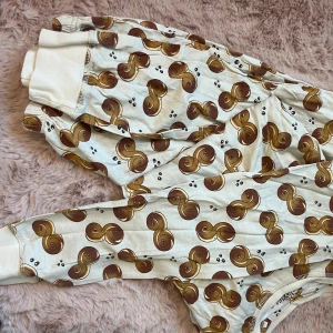 Pyjamas med lussebulle-mönster - Supermysig pyjamas i ljusbeige med ett unikt lussebulle-mönster i brunt och gult. Pyjamasen har resår i midjan och vid bensluten för extra komfort. Perfekta för chill dagar hemma eller när du vill sticka ut med ett roligt print.