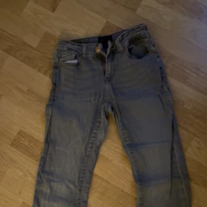 Grå jeans från ONLY X OU - Säljer ett par grå jeans från ONLY X OU med klassisk femficksdesign och raka bakfickor. Jeansen har en snygg tvättad look och är tillverkade i mjukt jeanstyg. Midwaist - lowwaist skulle jag säg.