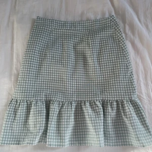 Rutig volangkjol  - Supersöt kjol från New Look i ljusgrönt och vitt rutigt mönster. Kjolen har volang nertill och stängs med dragkedja i sidan. Aldrig använd!