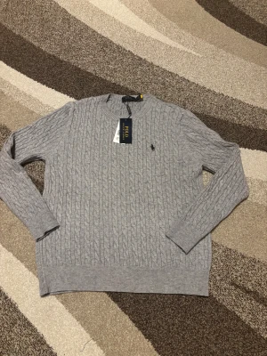 Polo Ralph Lauren flätad tröja - Säljer nu denna Polo Ralph Lauren flätade tröja som jag fick i present då den är väldigt liten i storlek en vad den borde vara. Tröjan ska vara storlek XXL men är mer som en M/L. Jag tror detta beror på materialet då det är bomull. Men den är helt ny aldrig använt och super fin. Vid frågor är det bara att skriva.