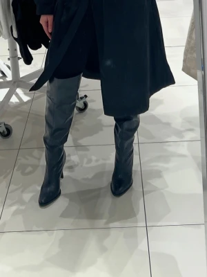 Zara-Svarta höga stövlar med klack - Säljer ett par svarta, höga stövlar med snygg klack och spetsig tå. Stövlarna är tillverkade i skinn och har en elegant, slät yta som ger en cool och stilren vibe. Nypris 1200kr