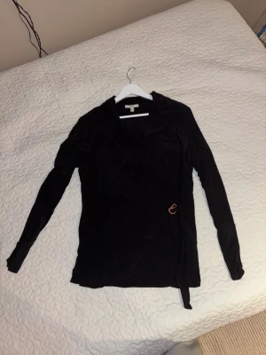 Exklusiv blus/topp från HOUSE OF DAGMAR - Exklusiv och fin svart blus från Dagmar i 100% Viscose, mjukt, glansigt material. Långärmad modell med knyt i sidan och en liten metallring som detalj. Perfekt för dig som gillar stilrena plagg med en twist. Perfekt för utgång eller finmiddag. Nypris 3400 kronor Använd fåtal gånger, inga tecken på slitage eller användning