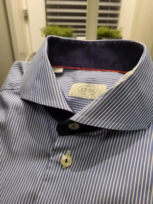 Blårandig skjorta från Eton slim fit - Snygg blårandig skjorta från Eton i slim fit-modell. Skjortan har klassisk krage med mörkblå insida och röda detaljer, vita knappar och långa ärmar med manschett. Tillverkad i mjuk bomull för en clean och fräsch look.