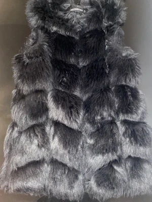 Svart pälsväst från Pecaocun - Säljer en fluffig svart pälsväst från Pecaocun i storlek S. Västen har en cool, chunky look med breda, mjuka sektioner och stängs med diskreta hyskor. Perfekt för dig som vill ha en statement piece till höst eller vinter.