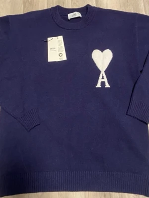 Marinblå stickad tröja - Snygg marinblå stickad tröja  med vit hjärtlogga och bokstaven A på bröstet. Rund hals och ribbade muddar vid ärmslut och nederkant. Perfekt för dig som gillar stilrena detaljer och vill ha något som sticker ut.