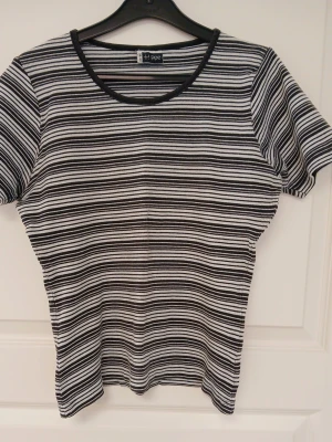 Svartvit randig topp - Randig topp i svart och vitt med rund halsringning och korta ärmar. Tillverkad i bomull och har en naturligt tvättad look. Se bilder för skick och passform. Färgen på bilderna, speciellt närbilderna, stämmer inte alltid överens med verkligheten. Storlek 38/40 enligt lappen. Armhåla till armhåla är cirka 45 cm. Axelsöm till ärmslut är cirka 18-19 cm. Tvättas i 40 grader.