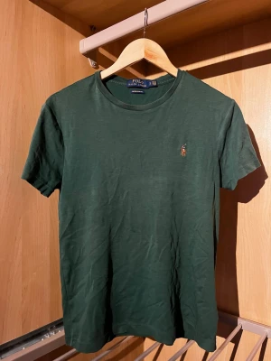 Grön t-shirt Polo Ralph Lauren - Snygg grön t-shirt från Polo Ralph Lauren i slim fit-modell. Klassisk rund hals och korta ärmar. T-shirten är i mjuk bomull och har den ikoniska broderade polospelaren på bröstet. Perfekt för dig som gillar stilrena och tidlösa plagg.