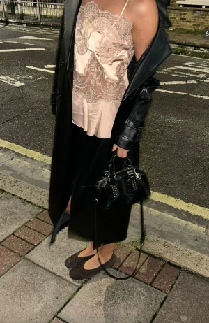 Beige satintopp med spetsdetaljer - Supersnygg beige satintopp (HELT SLUTSÅLD) med tunna axelband och romantiska spetsinfällningar framtill. Toppen har en lätt volang nedtill och v-ringad hals. Perfekt för dig som gillar en feminin och trendig look med lyxig känsla.