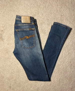 Nudie Jeans Tight Long John - Snygga blå jeans från Nudie Jeans, modell Tight Long John Super Blue. klassisk femficksdesign och coola orangea sömmar samt broderade bakfickor. Materialet är 98% bomull och 2% elastan för extra stretch och komfort.