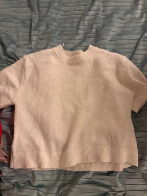 Vit stickad kortärmad tröja - Säljer en vit stickad tröja med korta ärmar och rund hals. Tröjan har ribbade detaljer vid halsringning, ärmslut och nederkant. Perfekt för dig som gillar enkel och clean stil. Passar till både jeans och kjol.