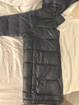 Svart dunjacka Peak Performance - Säljer en svart dunjacka från Peak Performance, modell JR Frost Down Jacket med Pertex Quantum-tyg. Jackan har quiltad design, huva och dragkedja framtill. Perfekt för kalla dagar och har en clean, sportig look.