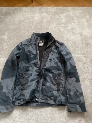 Camouflage vindjacka från G-Star RAW - Säljer en snygg vindjacka från G-Star RAW i mörkgrått och svart camomönster. 