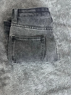 Gråsvarta ripped jeans med dip dye - Säljer ett par gråsvarta jeans med cool dip dye-effekt och slitna detaljer framtill. Jeansen har klassisk femficksdesign och raka ben. Materialet är en mix av bomull, polyester och viskos för skön passform.