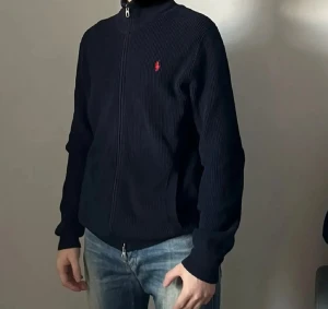 Mörkblå stickad kofta från Polo Ralph Lauren - Tröjan har dragkedja hela vägen. Mysigt och skönt material Väldigt bra skick, använda väldigt sparsamt. Storlek Medium.