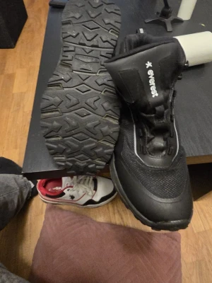 Svarta Everest kängor med snörning - Säljer ett par svarta kängor från Everest med grov sula och snörning. Skorna har en sportig look med meshdetaljer och reflekterande inslag längs sidan. Perfekt för dig som gillar outdoor och vill ha stabilitet och komfort.