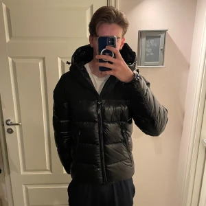 Svart pufferjacka från Replay - Säljer en svart pufferjacka från Replay med huva och dragkedja framtill. Jackan har blanka partier, två snedställda fickor med dragkedja och Replay-logga på ärmen. Perfekt för kalla dagar och riktigt snygg streetstil. Hör av vid frågor och funderingar!!!