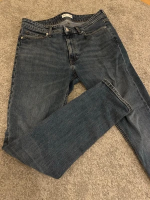 Slim fit blå jeans - Snygga slim fit jeans i mörkblå tvätt med klassisk femficksdesign och bruna sömmar. Jeansen har rak passform, normal midja och är tillverkade i mjukt bomullsjeansmaterial. Perfekt för dig som gillar stilrena och tidlösa jeans. Strl: W33 L34 slim fit. Modellen är 183cm, 72kg. Inga defekter. Hör av dig vid frågor.