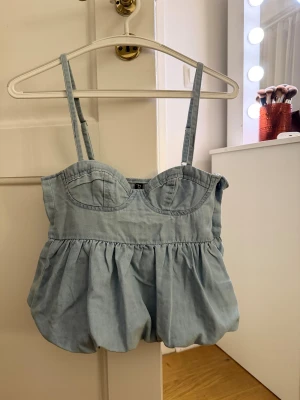 Ljusblå korsett-topp med volang - Supersöt ljusblå korsett-topp från h&m med tunna axelband och volang nedtill. Toppen har markerade kupor och en luftig, bubblig form som ger en cool och trendig vibe. 