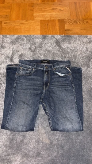 Replay blå jeans straight fit - Snygga blå jeans från Replay med klassisk femficksdesign och raka ben. Jeansen har normal passform, tydliga slitningar och kontrastsömmar. Märkespatch baktill och metallknapp framtill. Perfekta för dig som gillar stilrena och tidlösa jeans.