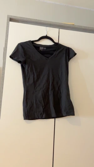 Svart v-ringad t-shirt Basic You XS - Svart t-shirt från Basic You i ekologisk bomull. Modellen är v-ringad och har korta ärmar. Enkel och stilren design som passar till det mesta. Perfekt basplagg i garderoben.