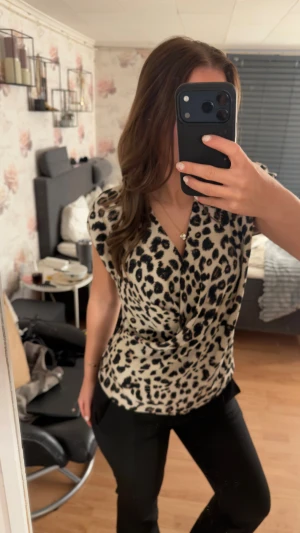 Leopardmönstrad omlottblus i beige - Säljer en snygg omlottblus med leopardmönster i beige och svart. Blusen har korta ärmar och ett v-format omlottliv som ger en cool och trendig look. Perfekt för dig som gillar djurmönster och vill sticka ut lite extra.