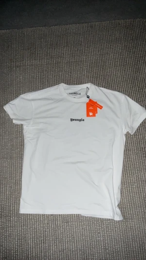 Vit t-shirt från YoungLA - Vit t-shirt från YoungLA med svart logga tryckt på bröstet. Klassisk rund halsringning och korta ärmar. Helt ny kvitto fins.