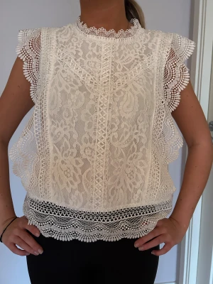 Vit spetsblus med spetsdetaljer - Supersöt vit blus i spets med blommigt mönster och volangkantade ärmar. Krage med dekorativ spets och har fina detaljer längs nederkant och axlar. 🤍🤍