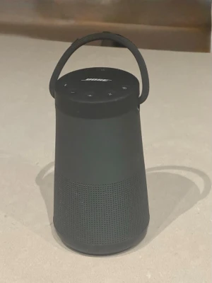 Bose SoundLink Revolve+ Bluetooth-högtalare - Bose SoundLink Revolve+ bärbar Bluetooth-högtalare med 360° ljud, robust handtag och enkel kontrollpanel. Levereras med original laddare. Svart färg, i gott skick utan synliga skador eller slitage. Perfekt för både inomhus- och utomhusbruk. Orginal laddare från Bose medföljer.
