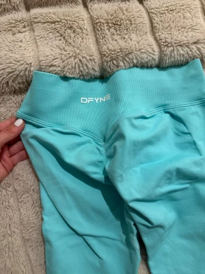 Turkosa leggings från DFyne - Snygga turkosa leggings från DFyne med hög midja och bred ribbad linning. Perfekta för träning eller chill, sitter tajt och följer kroppen. Materialet är stretchigt och mjukt för maximal komfort.